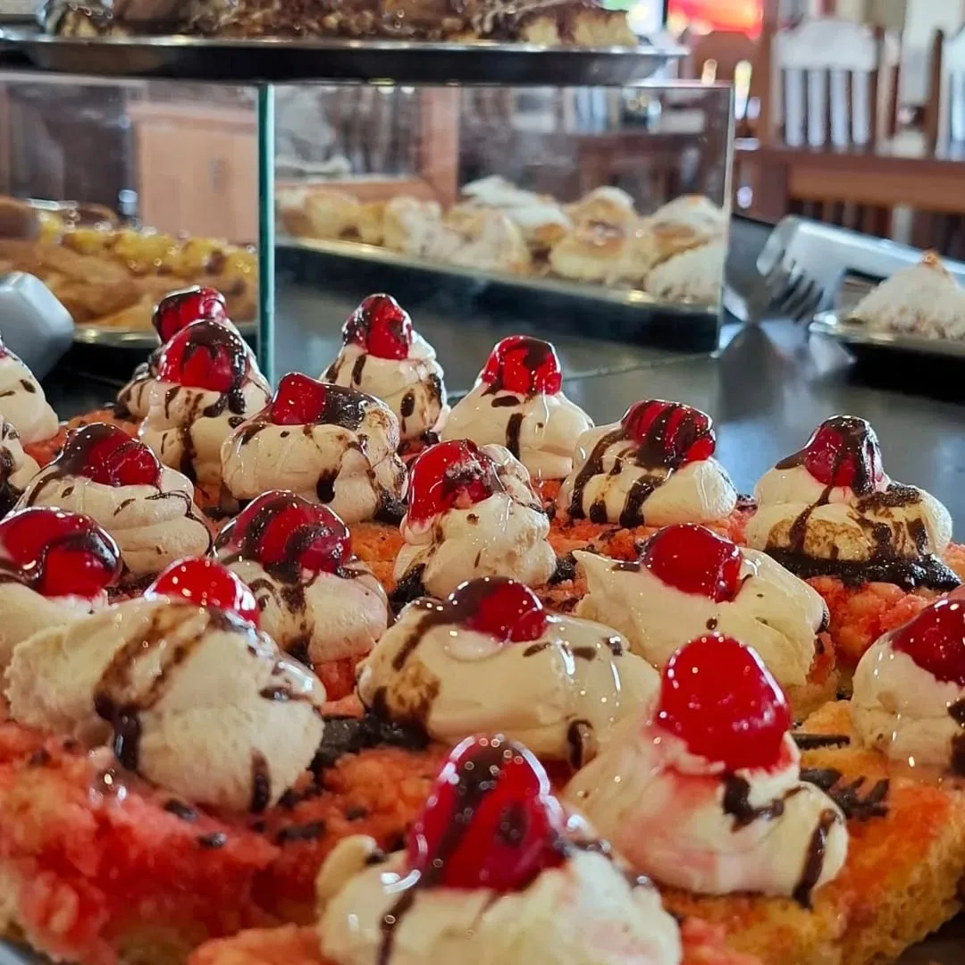 Espacio representativo del hotel: Una vitrina de pastelería muestra dulces cubiertos de crema, chocolate y cerezas rojas.