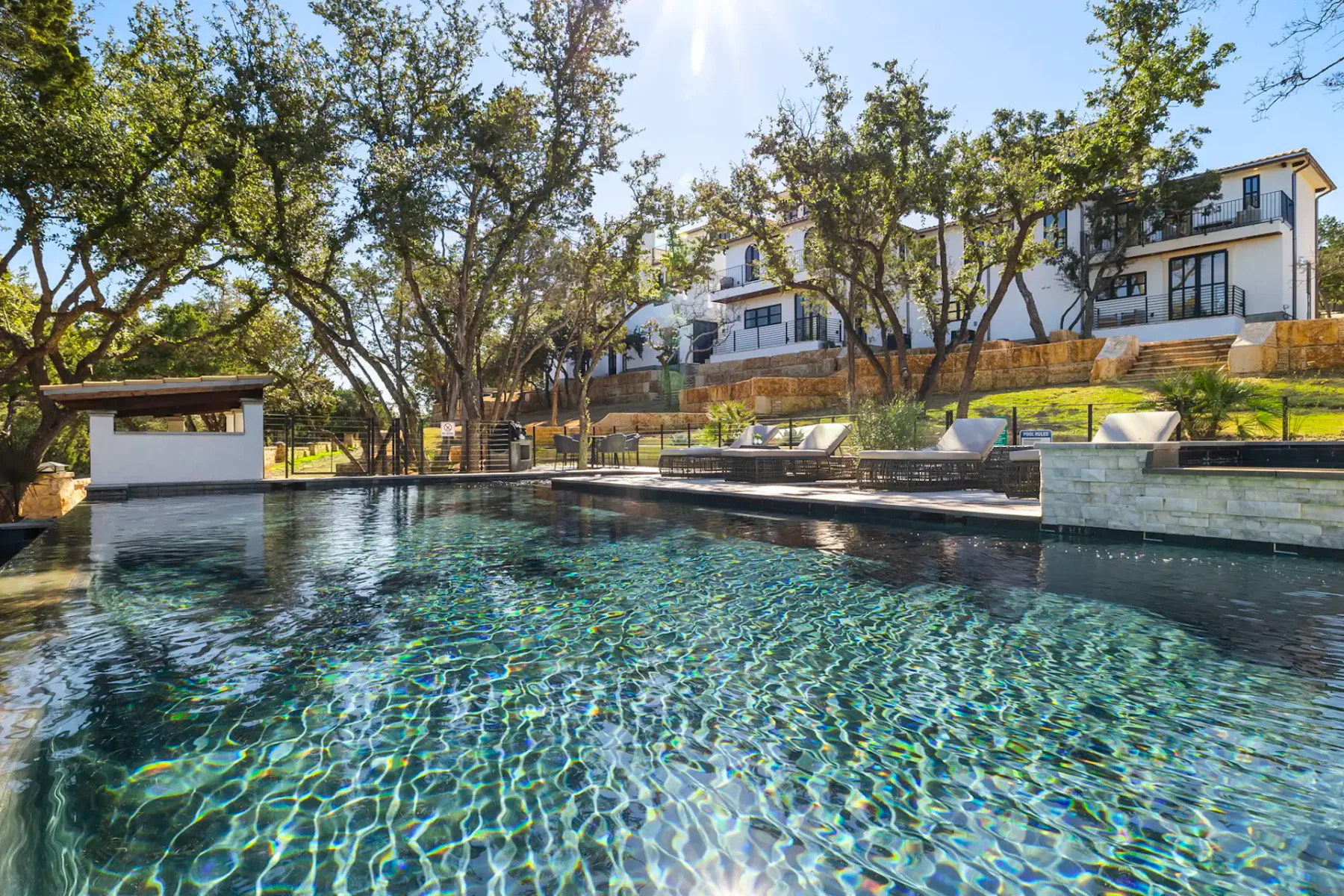 Shared amenity: Outdoor swimming pool beside trees, lounge seating, and modern buildings.