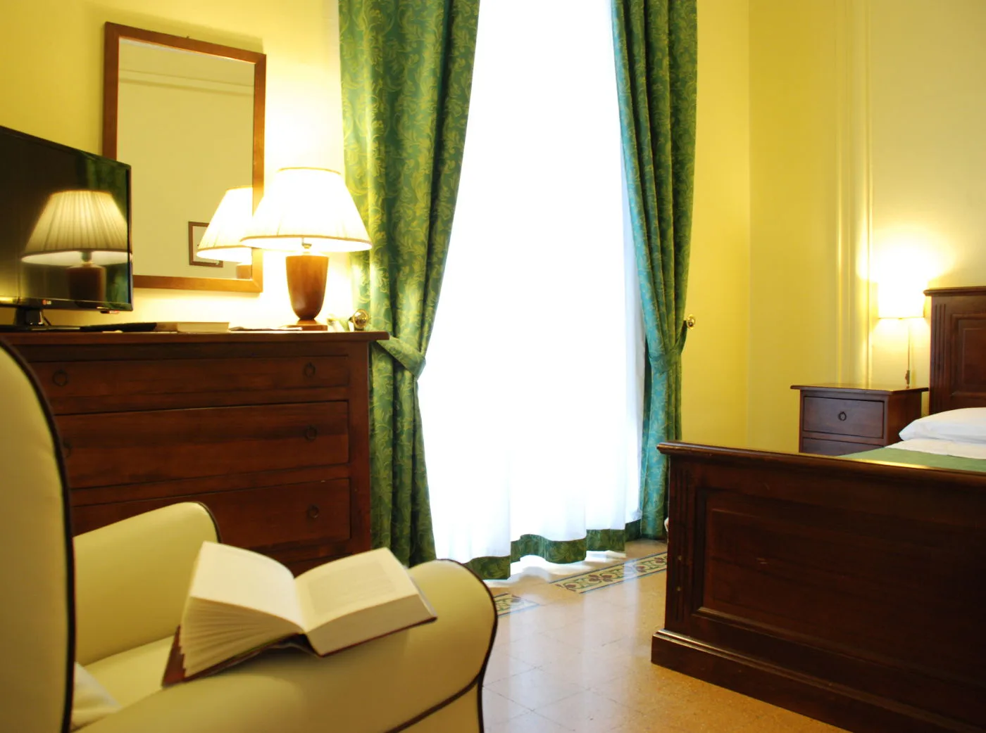 Representative hotel space: A bedroom with dark wooden furniture, lamps, and an open book.