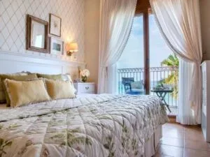 Representative hotel space: A bedroom with a large bed beside curtained windows opening onto a balcony.