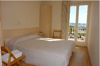 Espacio representativo del hotel: Un dormitorio con una cama, un armario y puertas de cristal que dan a un balcón.