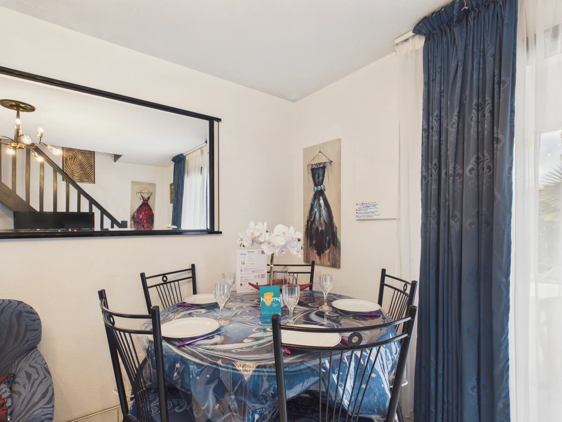 A dining area with a round table set with dishes beside a large mirror.