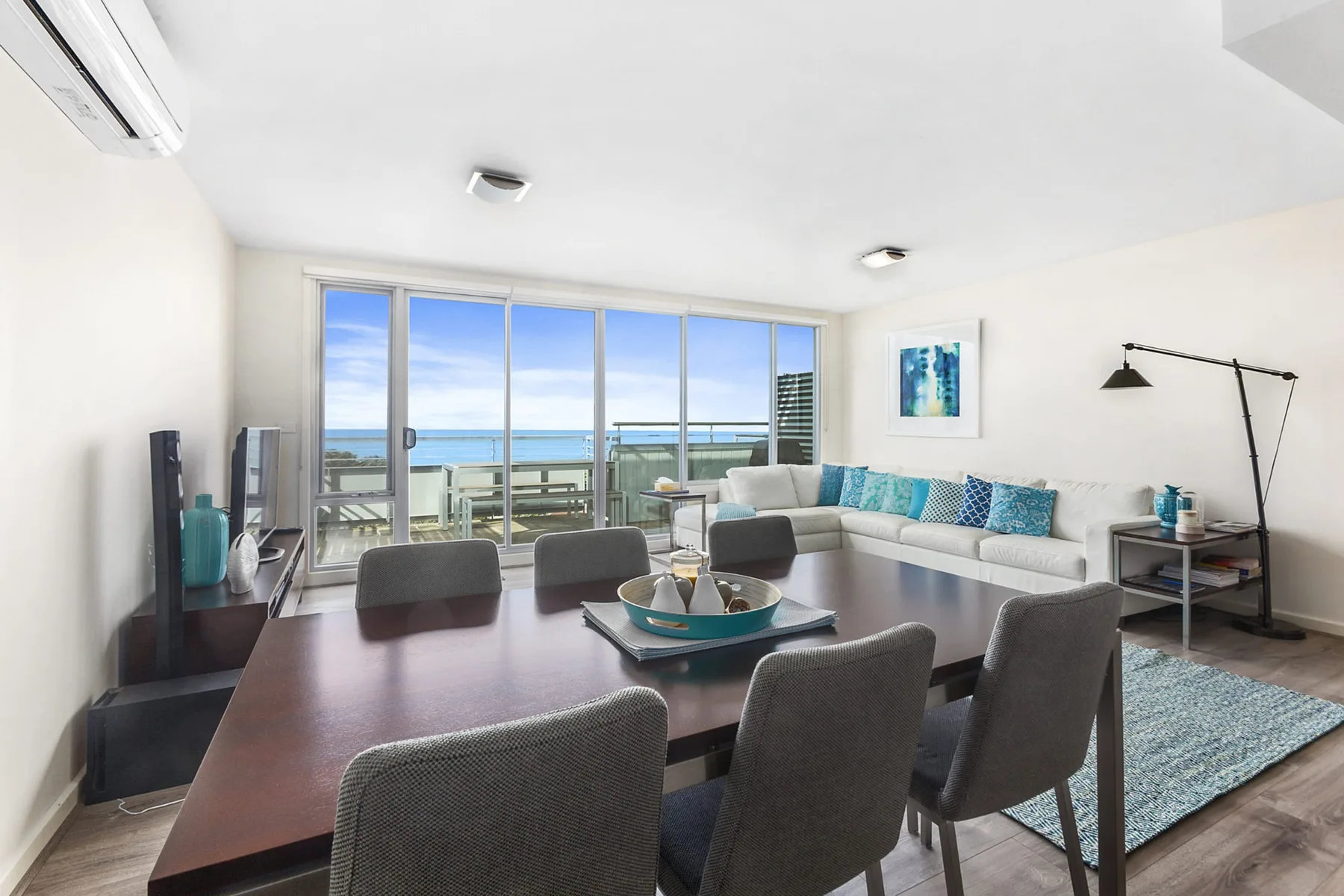 A bright living and dining area opens onto a balcony with ocean views.