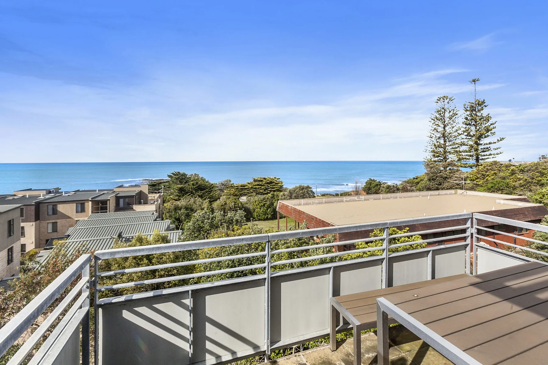 A balcony overlooks the ocean, nearby buildings, and coastal greenery.
