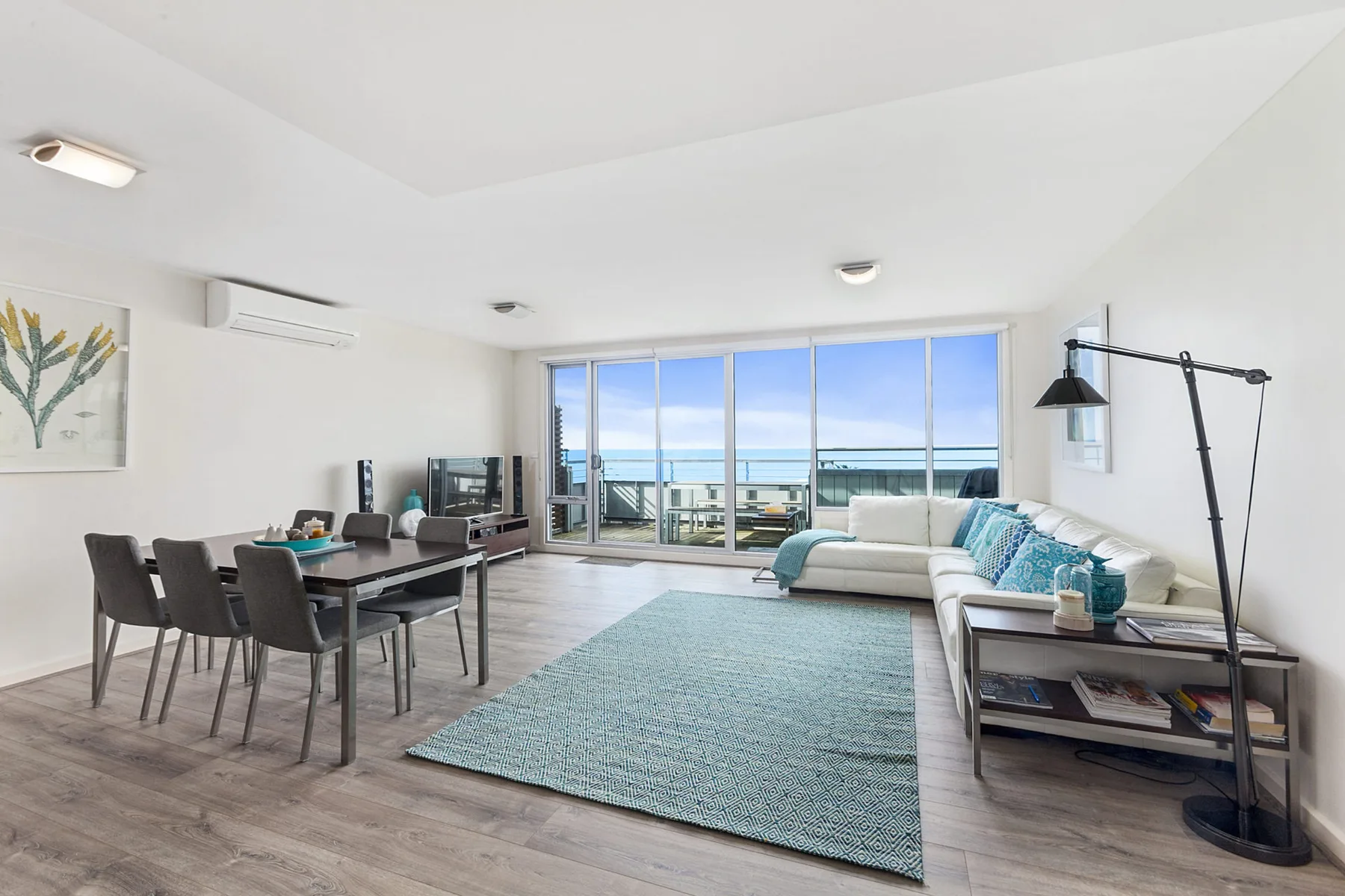 A bright open-plan living and dining area opens onto a balcony with ocean views.