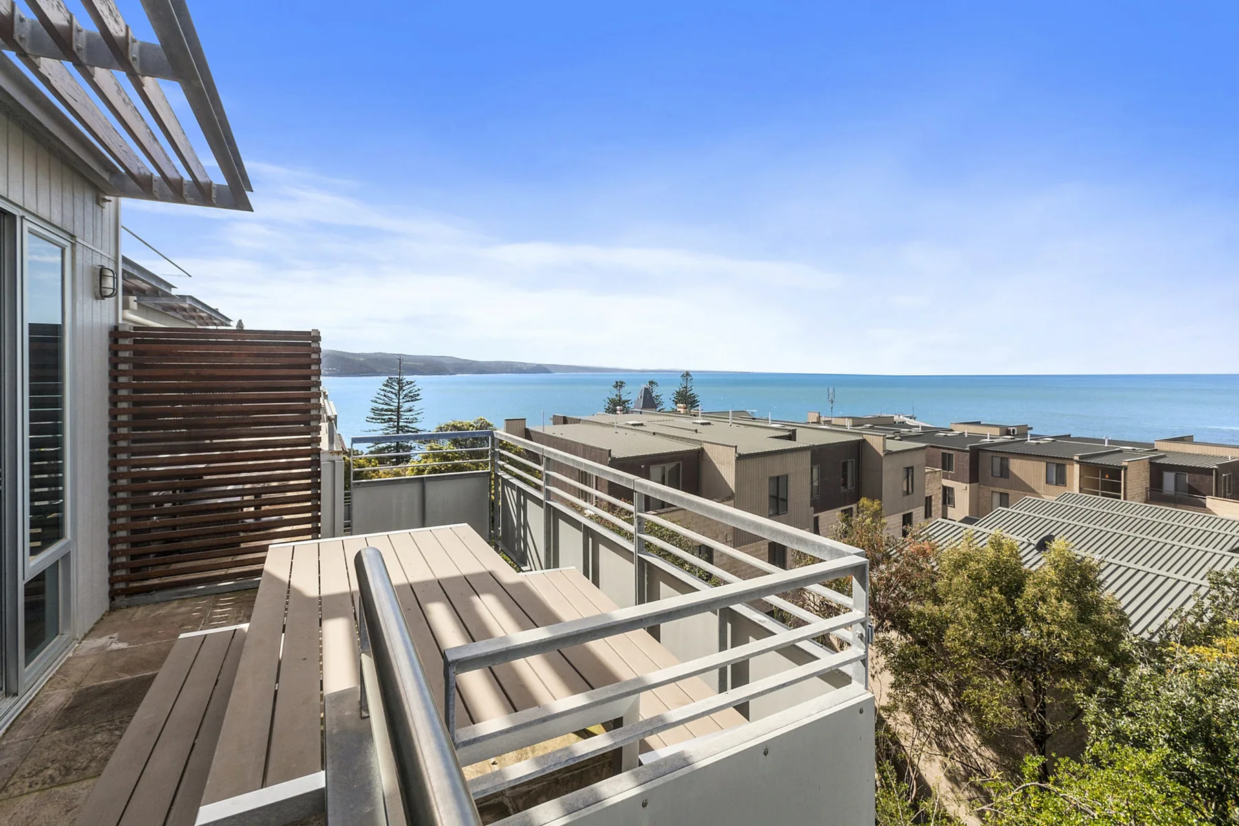 A balcony with railing overlooks nearby buildings and the ocean.