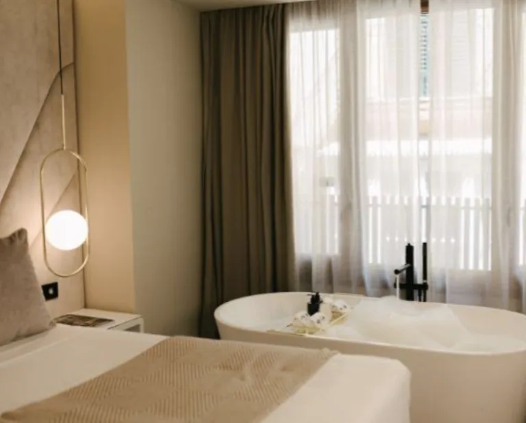 Representative hotel space: A bedroom with a bed beside a freestanding bathtub and curtained window.