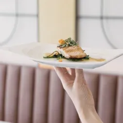 Representative hotel space: A plated meal is held above a table in a softly lit dining area.