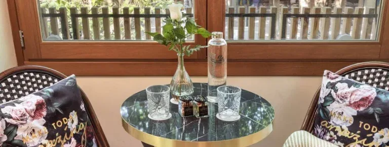 Representative hotel space: A small round table with glasses sits between two cushioned chairs by the window.