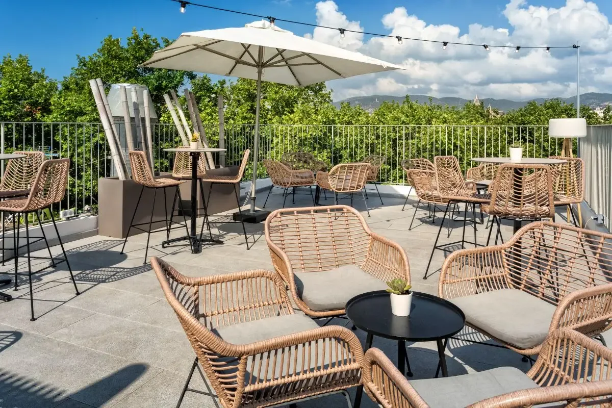 Representative hotel space: An outdoor terrace has woven seating, tables, and a large umbrella.
