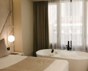 Representative hotel space: A bedroom with a bed beside a freestanding bathtub and curtained window.
