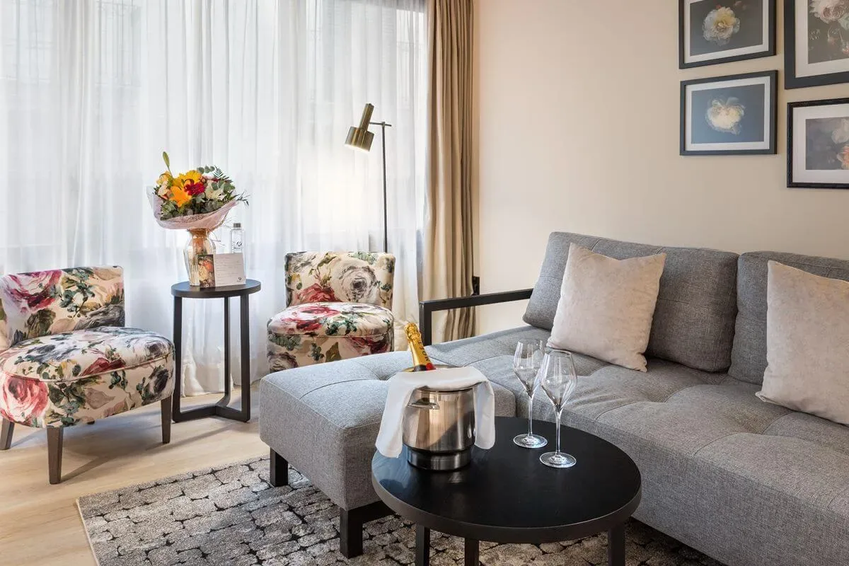 Representative hotel space: A living room with gray seating, floral chairs, and a coffee table.