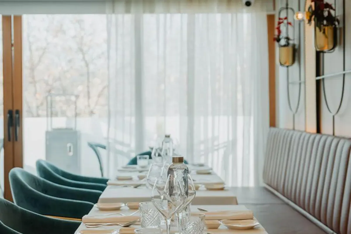 Representative hotel space: A dining table is set with glassware beside upholstered seating and sheer curtains.
