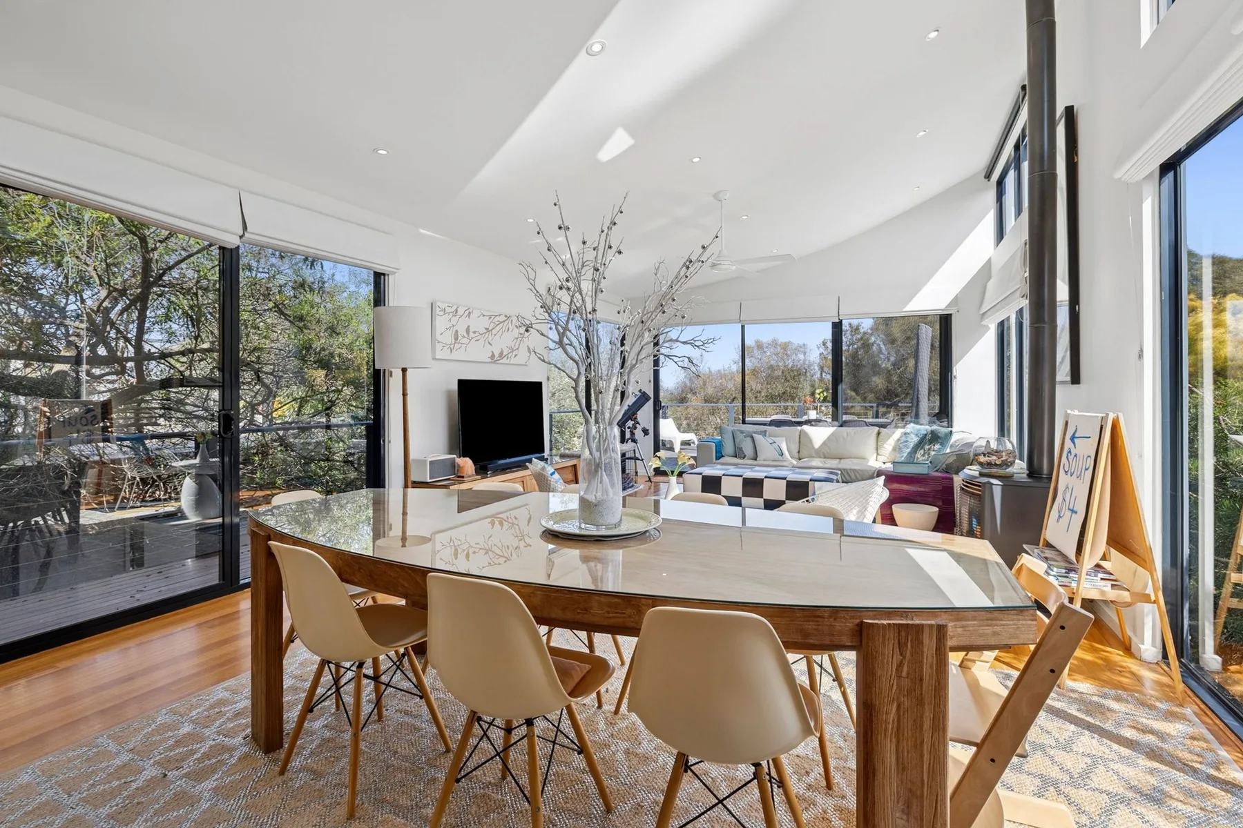 A bright open-plan living and dining area with large windows and a long dining table.