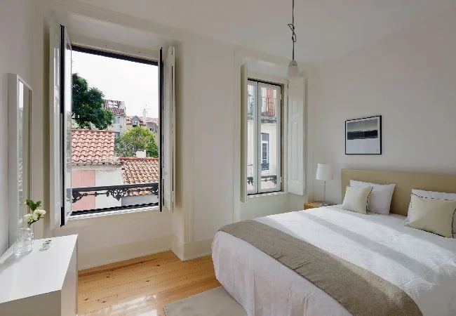 A bright bedroom with a neatly made bed and open windows.