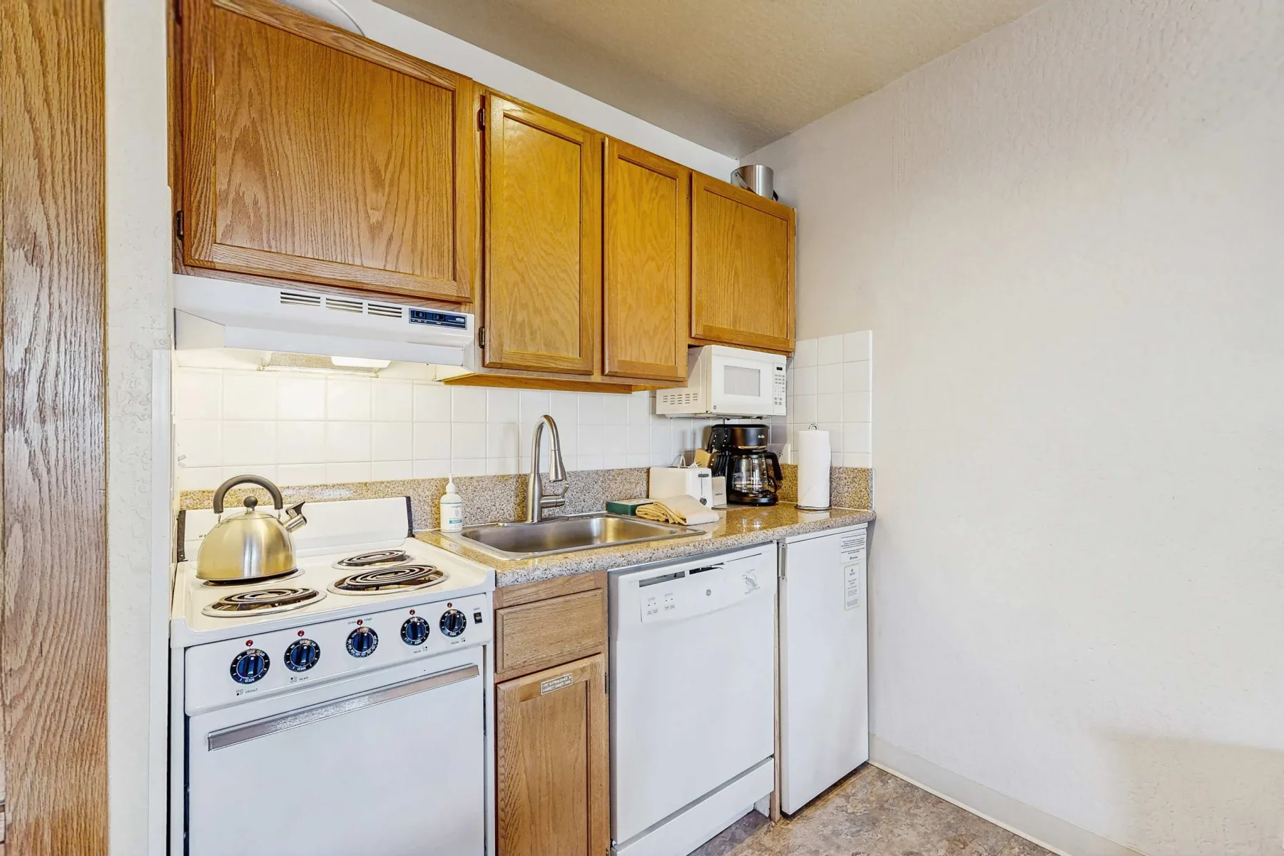 A compact kitchen with wooden cabinets, a stove, and a sink.