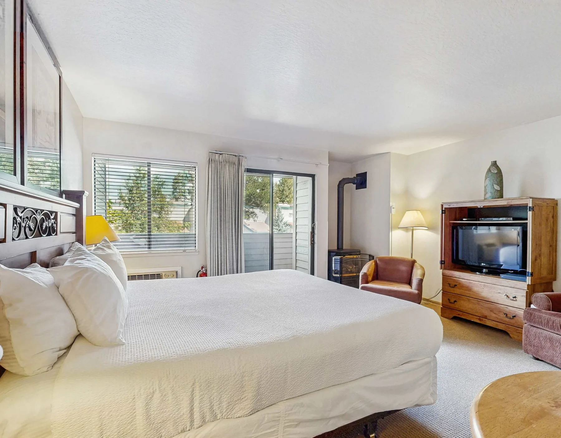 A bright bedroom with a large bed, windows, and a television on a wooden dresser.