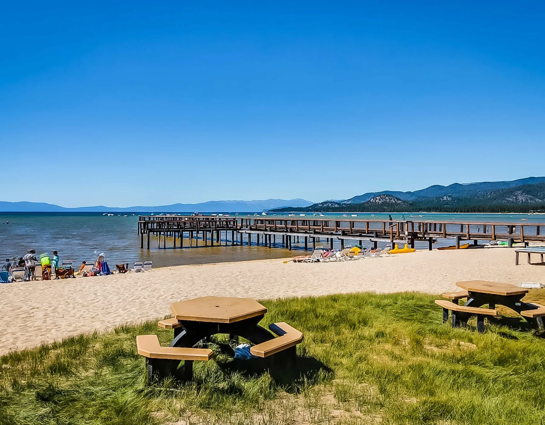 Shared amenity: A lakeside beach with a long wooden pier and picnic tables on the grassy shore.