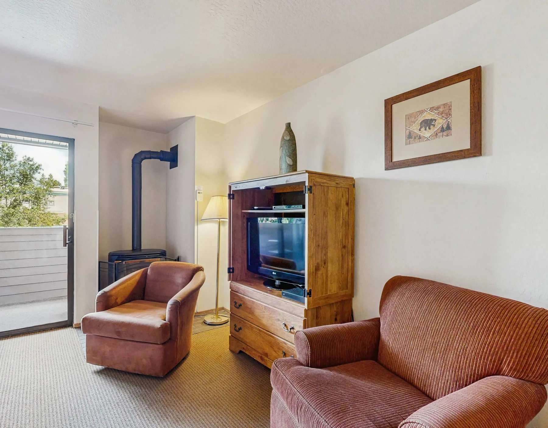 A living room with seating, a television, and a glass door opening to a balcony.