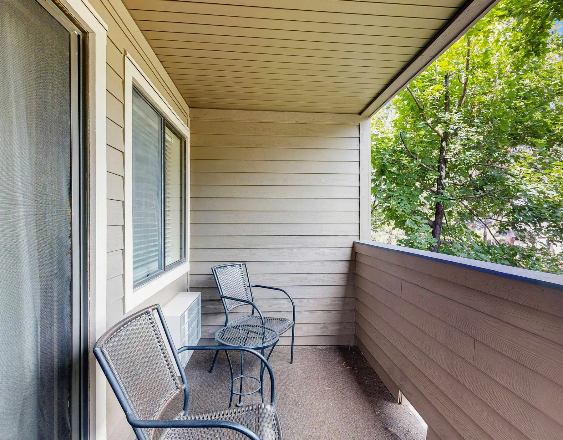 A covered balcony with metal seating and leafy trees visible beyond the railing.