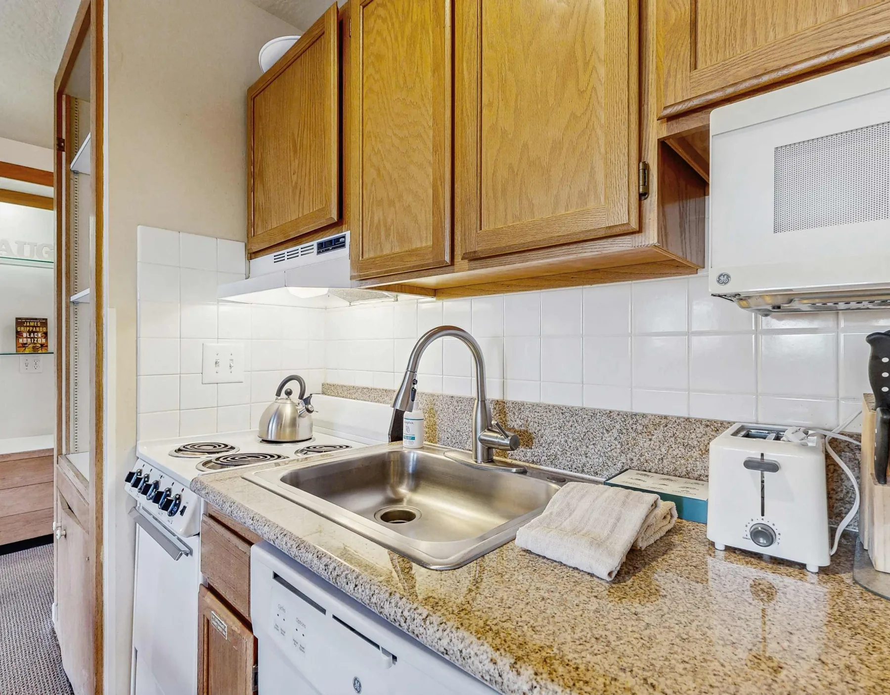 A kitchen counter with a sink, stove, and wooden cabinets.
