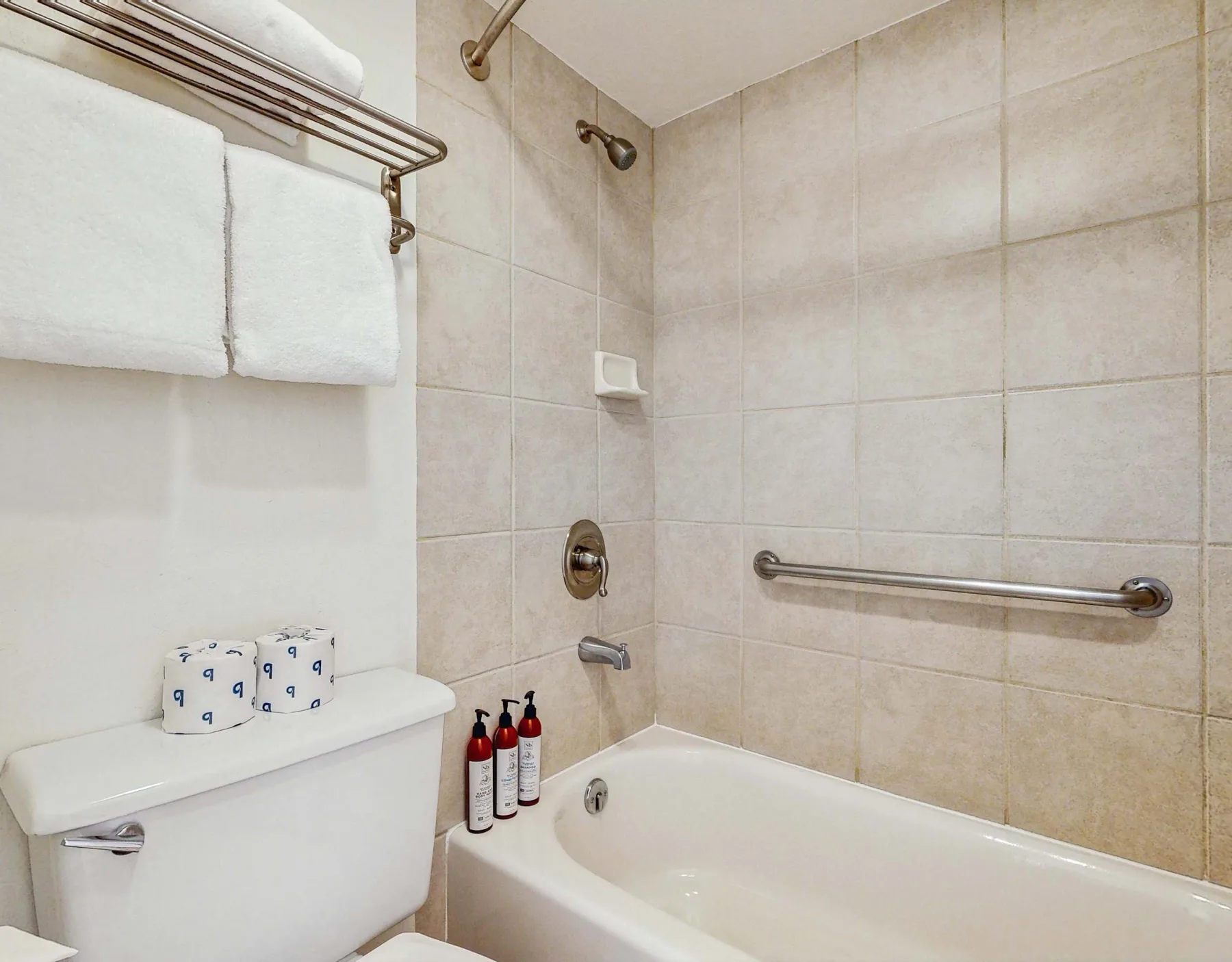 A tiled bathroom with a bathtub, grab bar, and towels.
