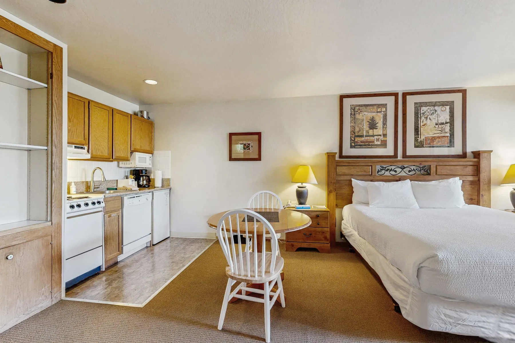 A bedroom with a bed and a compact kitchen area beside a small dining table.