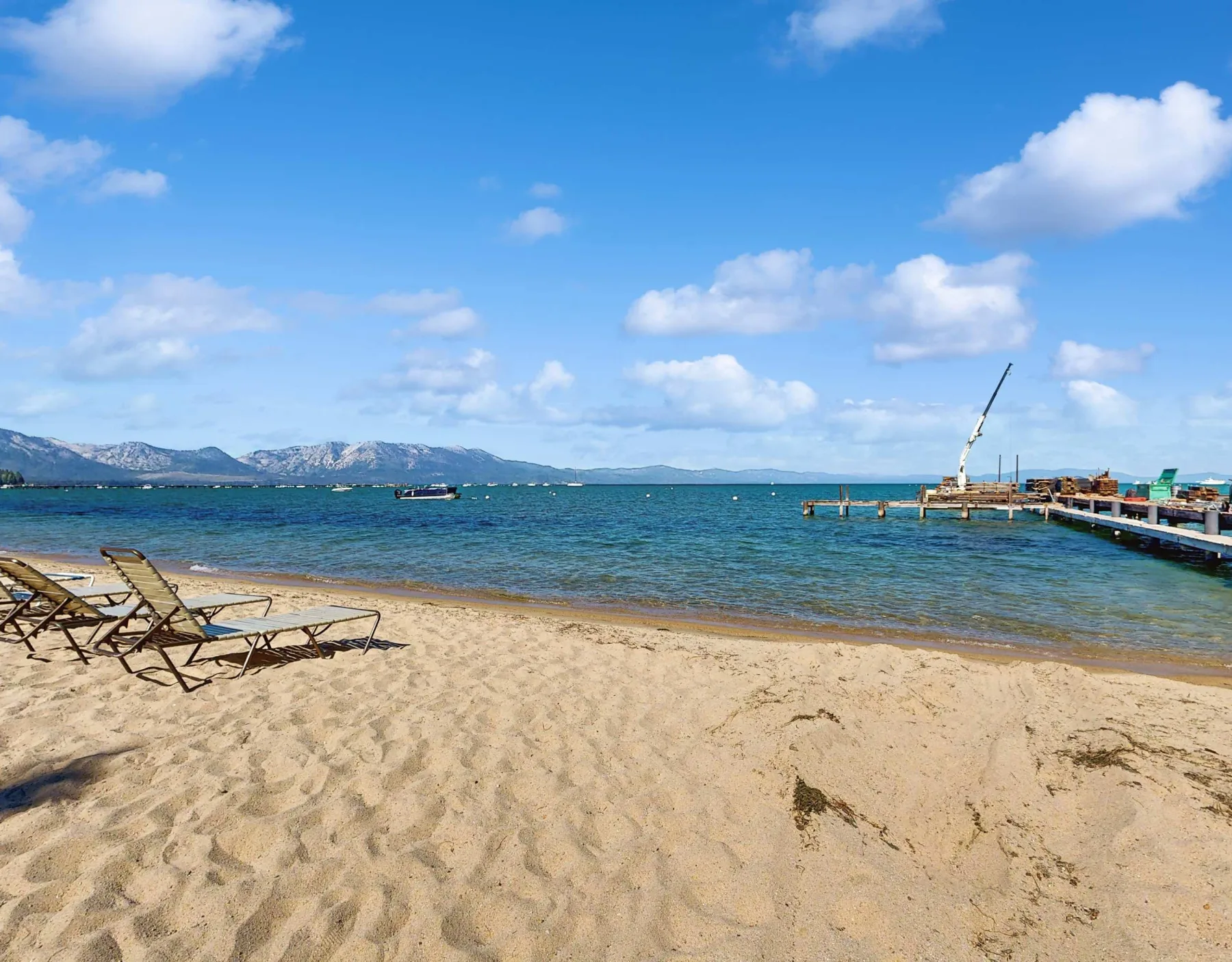 Shared amenity: A sandy beach with lounge chairs beside clear water and a pier.