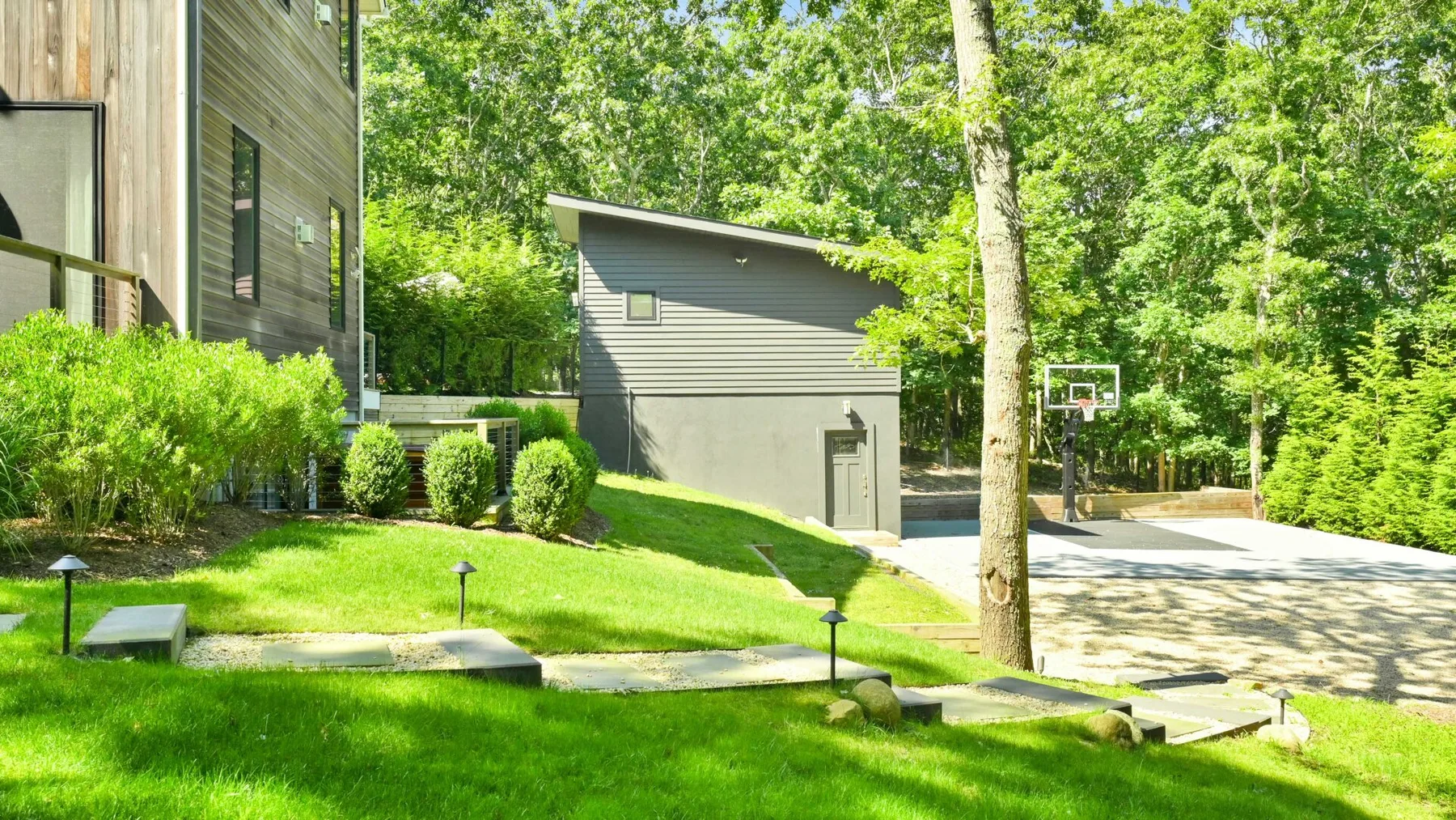 A landscaped outdoor area beside modern buildings, with trees and a paved path.