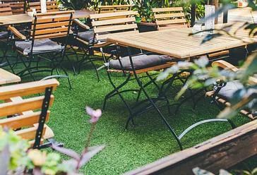 Representative hotel space: An outdoor seating area with wooden tables and chairs on green turf.