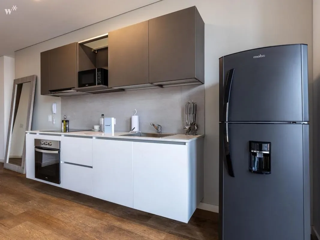 Una cocina moderna con gabinetes blancos inferiores, alacenas oscuras, un horno y un refrigerador grande.