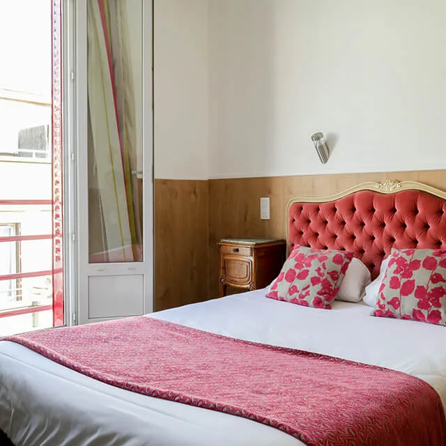 Representative hotel space: A bedroom with a bed featuring a red upholstered headboard and floral pillows.