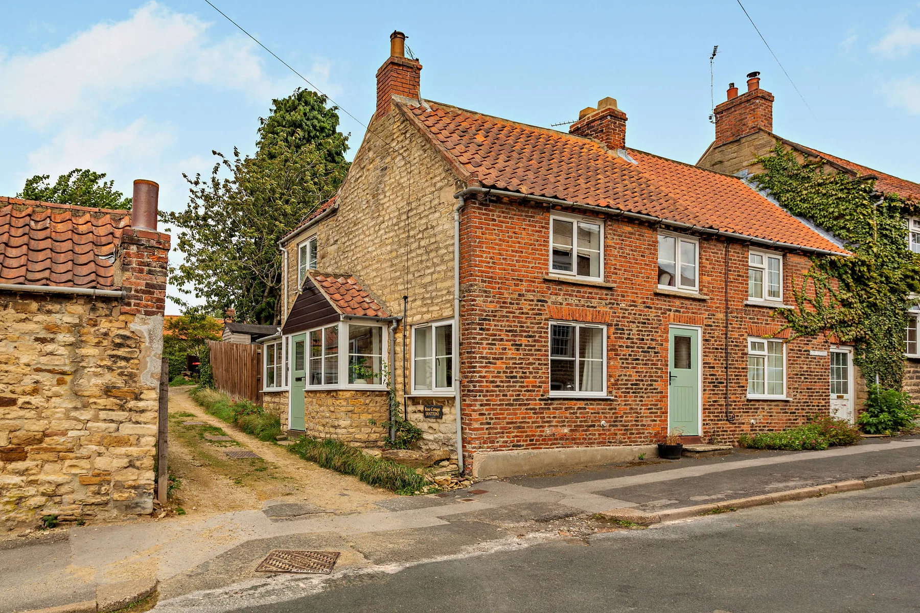 A brick-and-stone house stands beside a narrow lane and paved road.