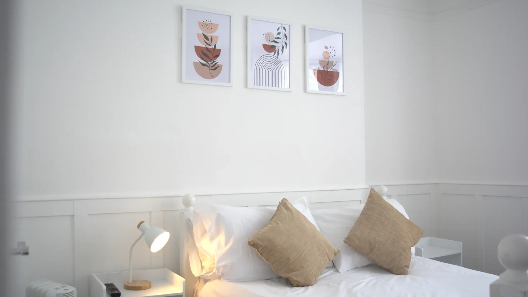 Representative hotel space: A bedroom with a neatly made bed and three botanical prints above it.