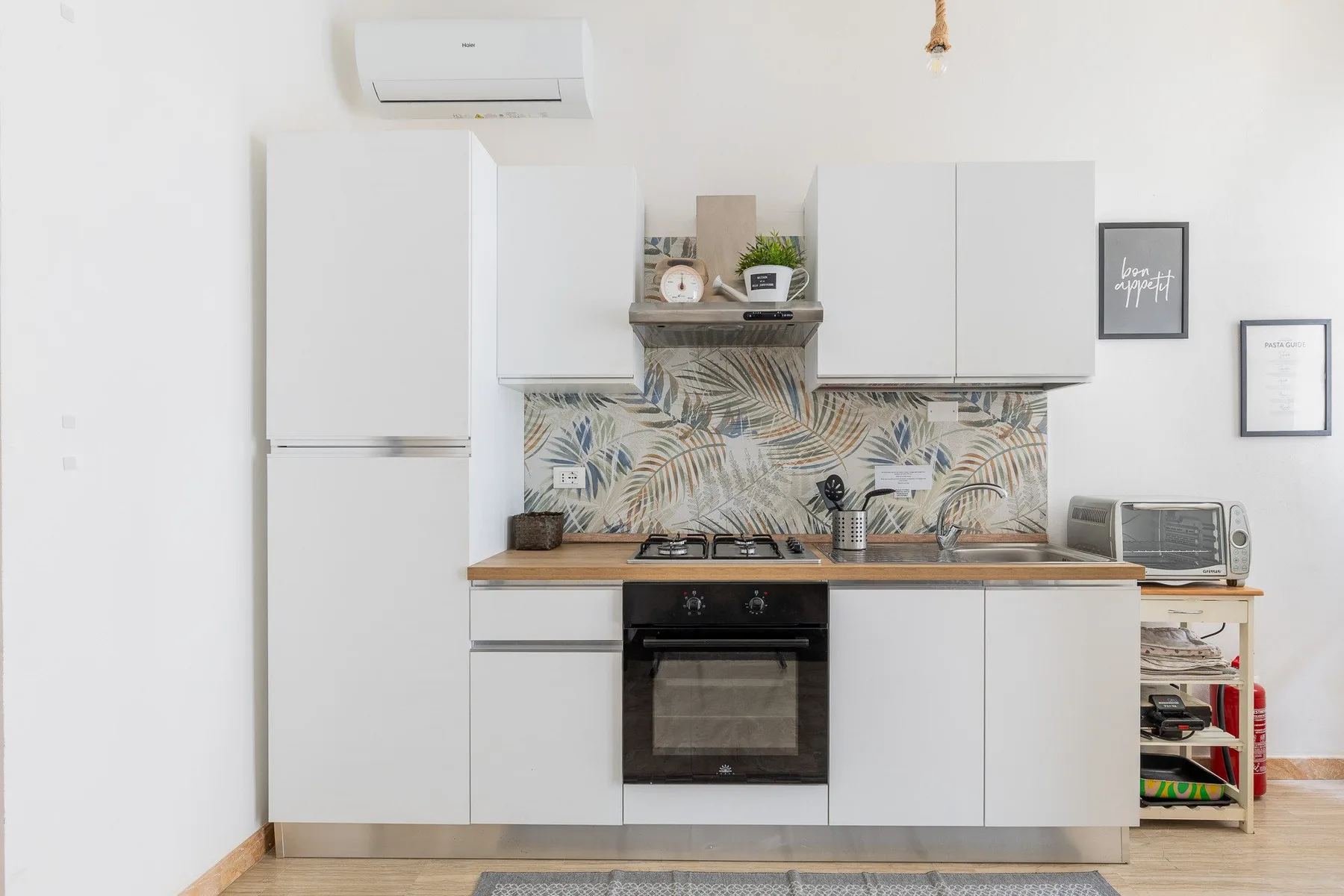 Una cocina compacta con gabinetes blancos, una estufa y un salpicadero estampado.