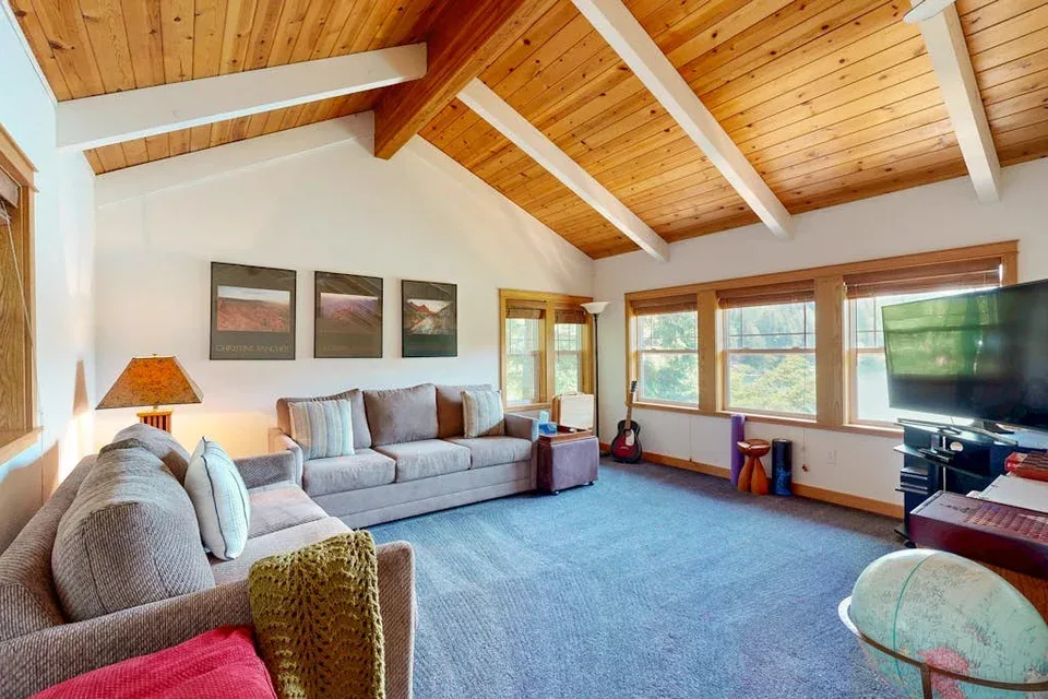 Una sala de estar con asientos, ventanas amplias y techo abovedado de madera.