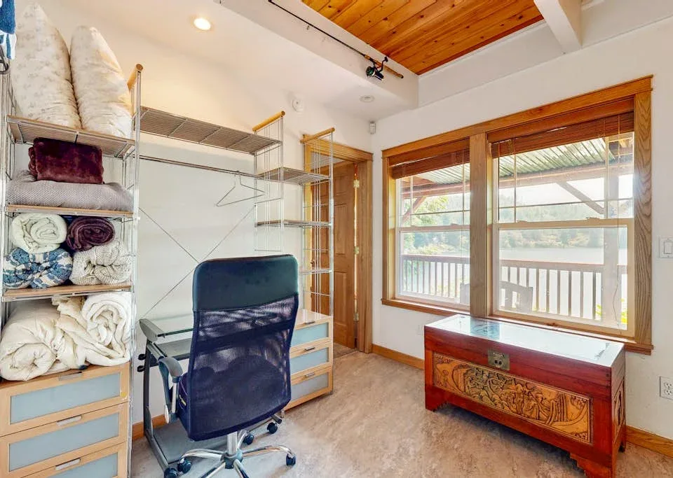 Una habitación luminosa con escritorio, estantes de almacenamiento y grandes ventanas con vista a un balcón.