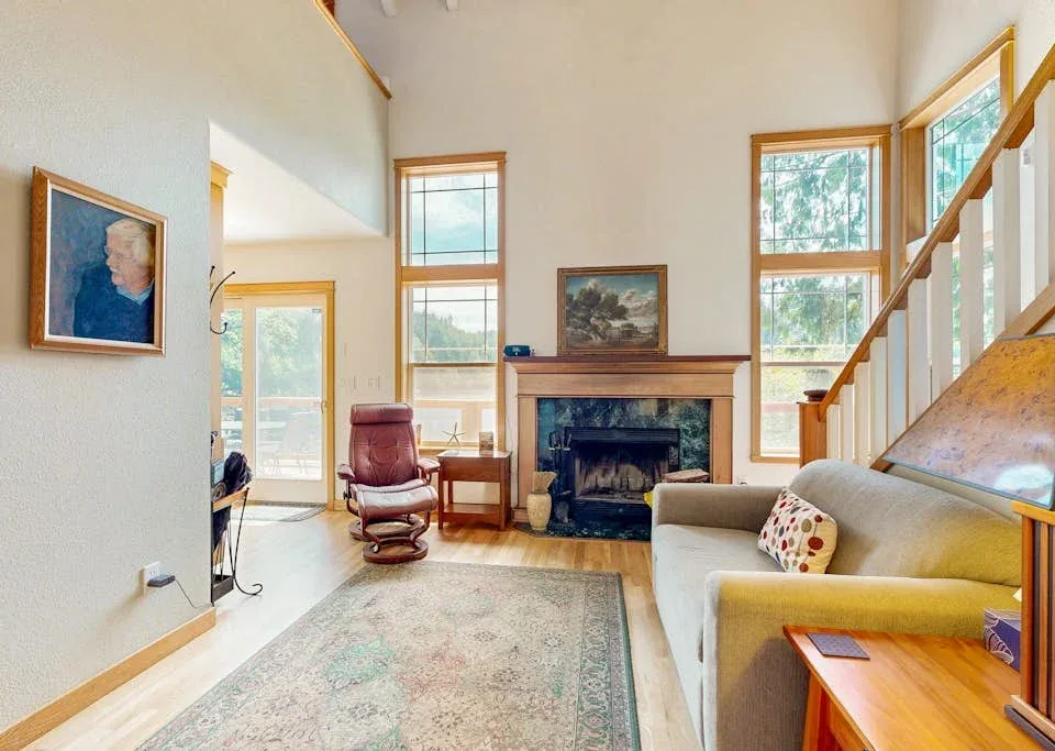 Una sala luminosa con chimenea, asientos y ventanas grandes.