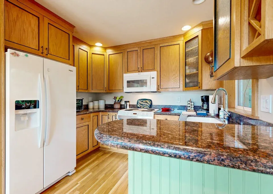 Una cocina con gabinetes de madera, un refrigerador y una isla curva con encimera de piedra.