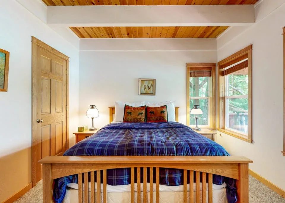Un dormitorio con una cama de madera, ropa de cama a cuadros y ventanas a un lado.
