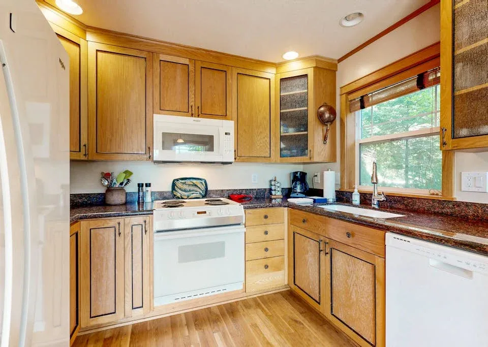 Una cocina con gabinetes de madera, electrodomésticos blancos y una encimera bajo una ventana.
