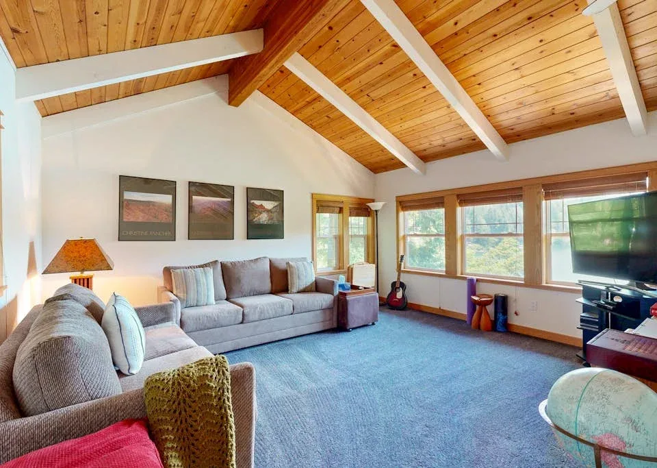 Una sala de estar con asientos bajo un techo alto de madera y ventanas grandes.