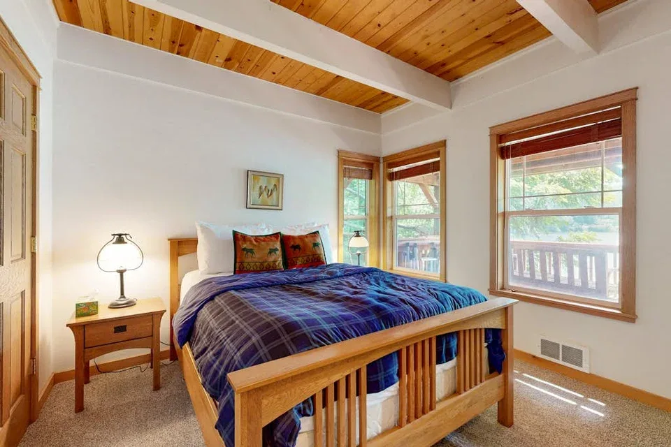 Un dormitorio con cama de madera, ropa de cama azul y ventanas con persianas.