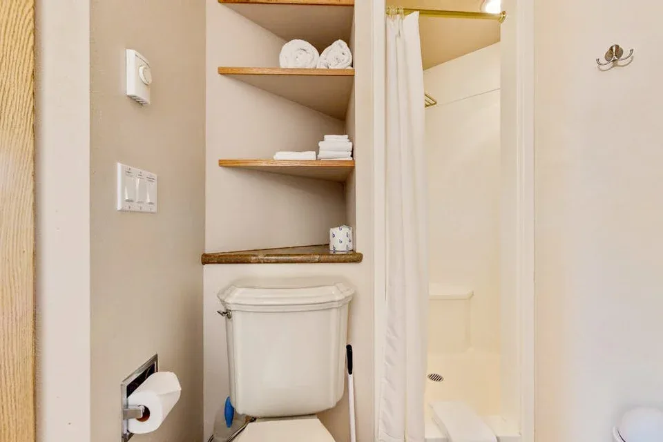 Un baño con un inodoro, estantes para toallas y una ducha con cortina.
