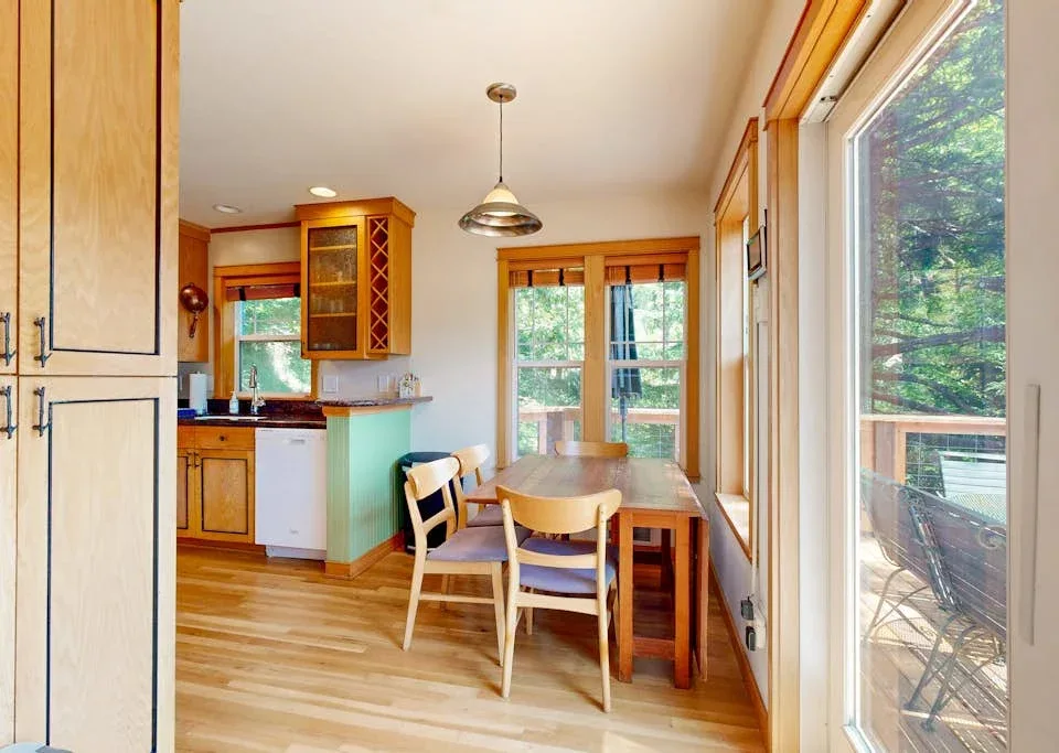Comedor con una mesa de madera y sillas junto a grandes ventanas.