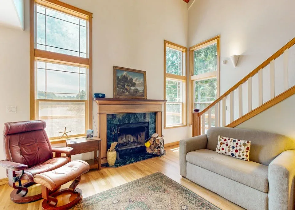 Una sala luminosa con chimenea, ventanas altas y asientos cómodos.
