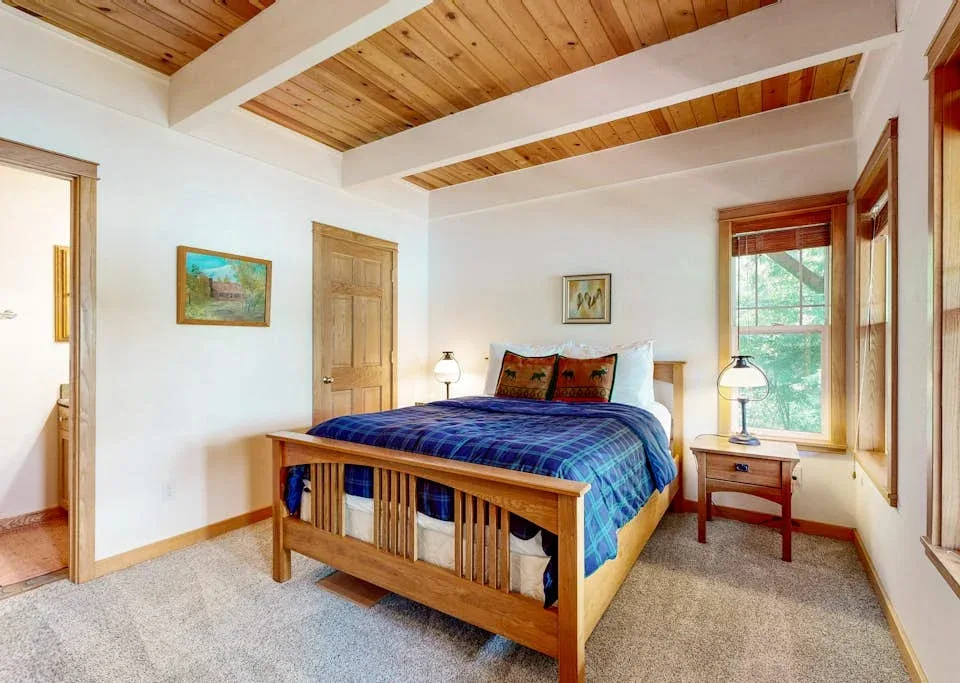 Un dormitorio con cama de madera, ropa de cama azul y ventanas con vista a la vegetación.