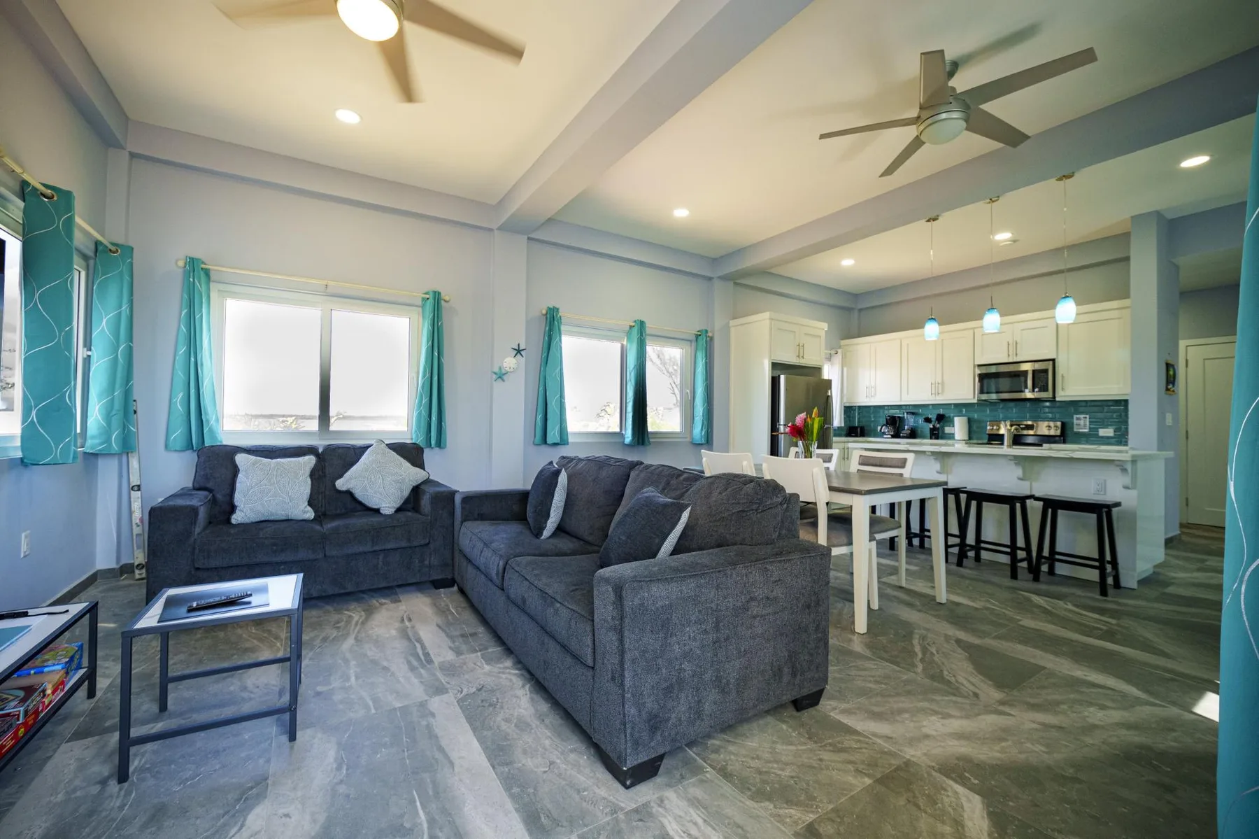 A living room with gray seating opens onto a kitchen and dining area.