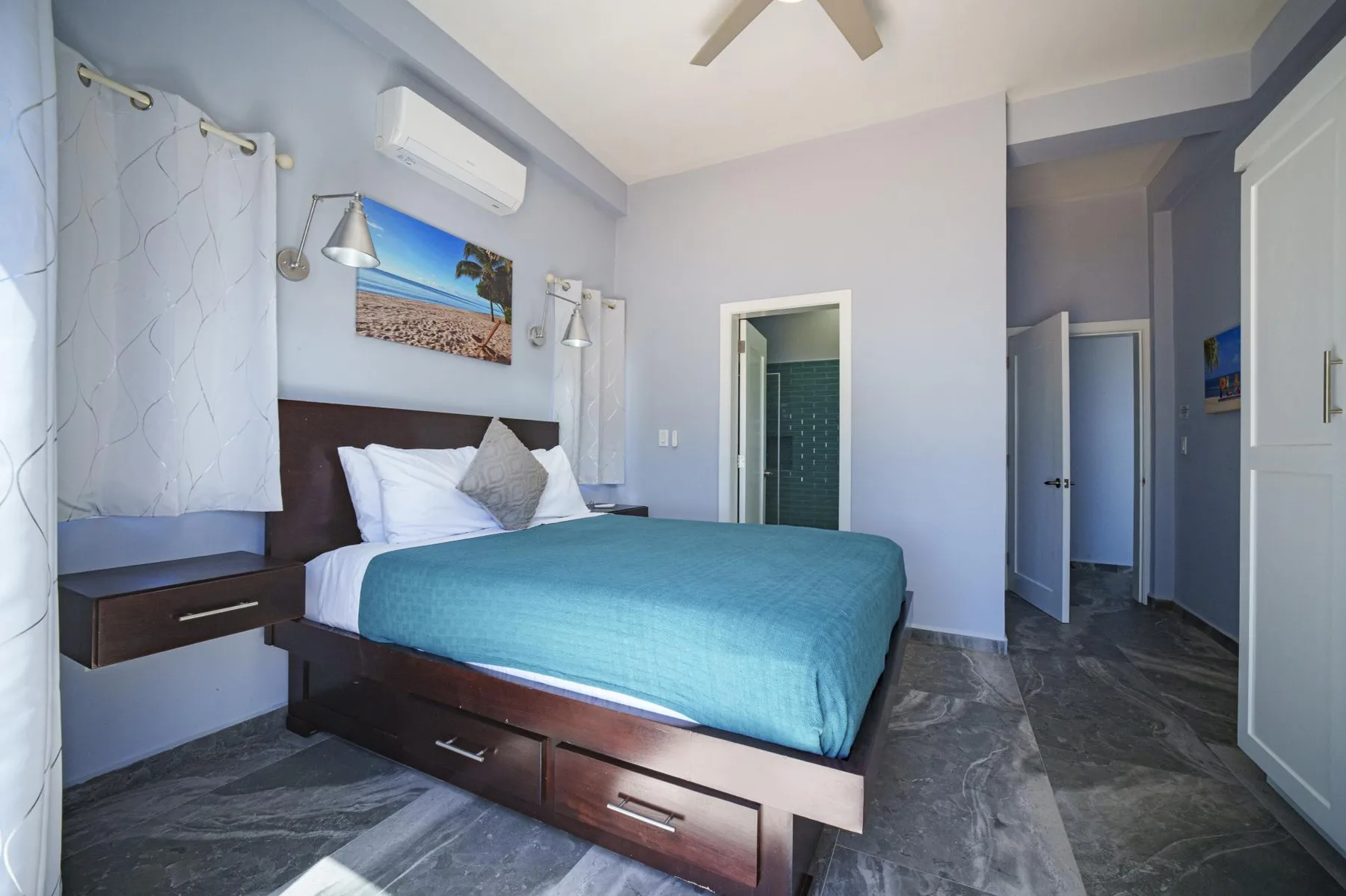 A bedroom with a bed covered in blue bedding and a doorway to a bathroom.