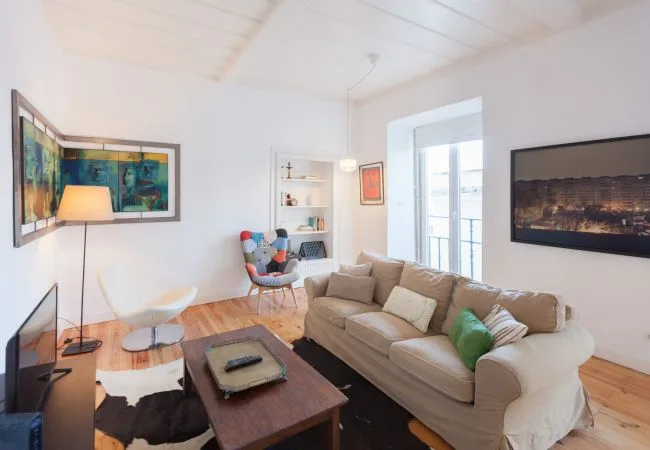 Una sala luminosa con un sofá beige, una mesa de centro y arte colorido en la pared.